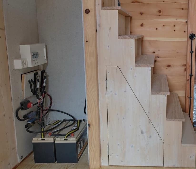 Zwei Batterien ermöglichen das Speichern von Energie. Ein Victron-Multiplus-Gerät ist an der Aussenwand installiert, welches das Laden der Batterien und die Umwandlung von 230V nach 12V (Licht, Kühlschrank, Komposttoilette) ermöglicht. Ein direkter Anschluss zu 230V ist ebenfalls vorhanden.
