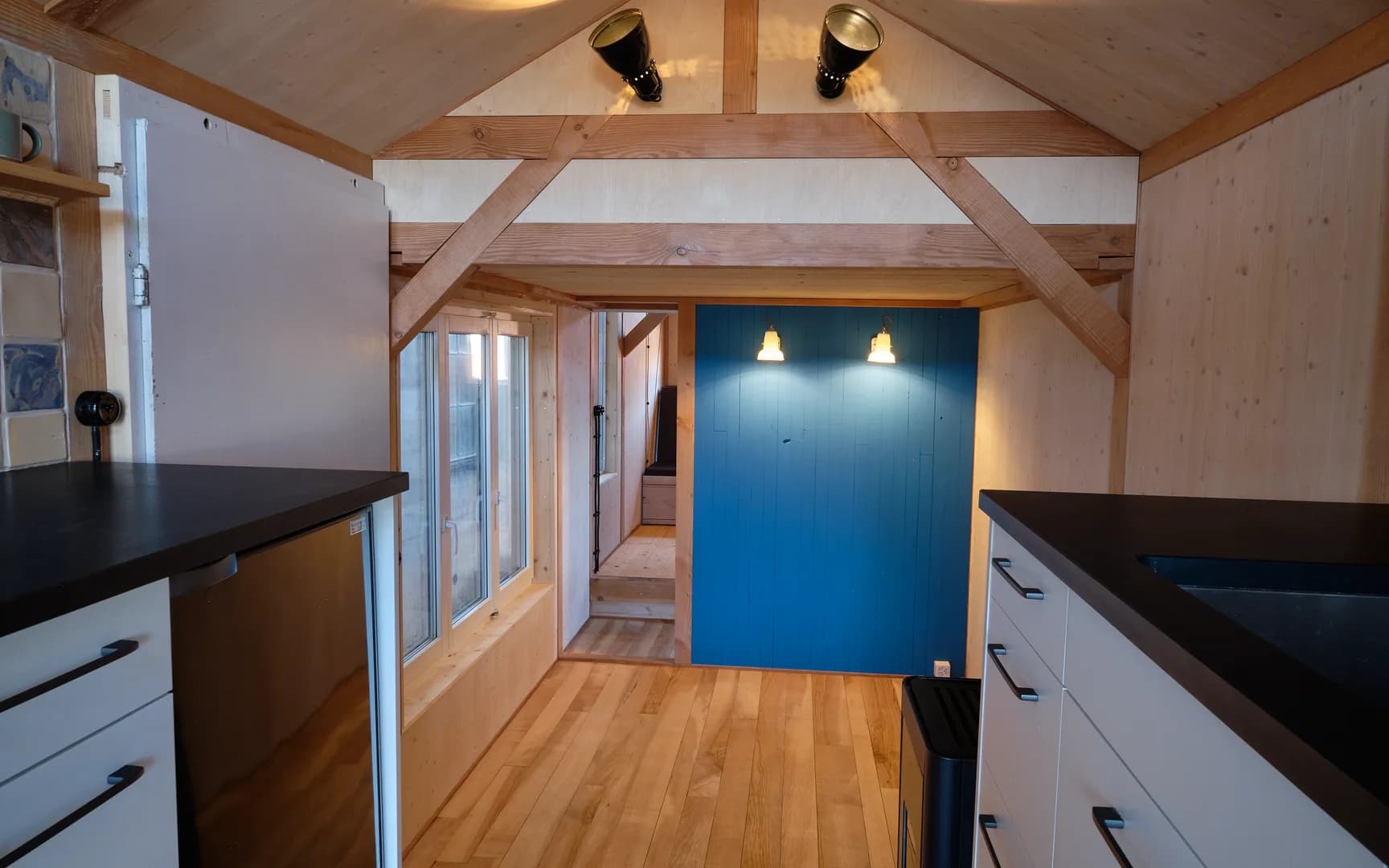 Blick durch das ganze Haus: Küche links, Gang mit Holzboden, blaue Wand am Ende