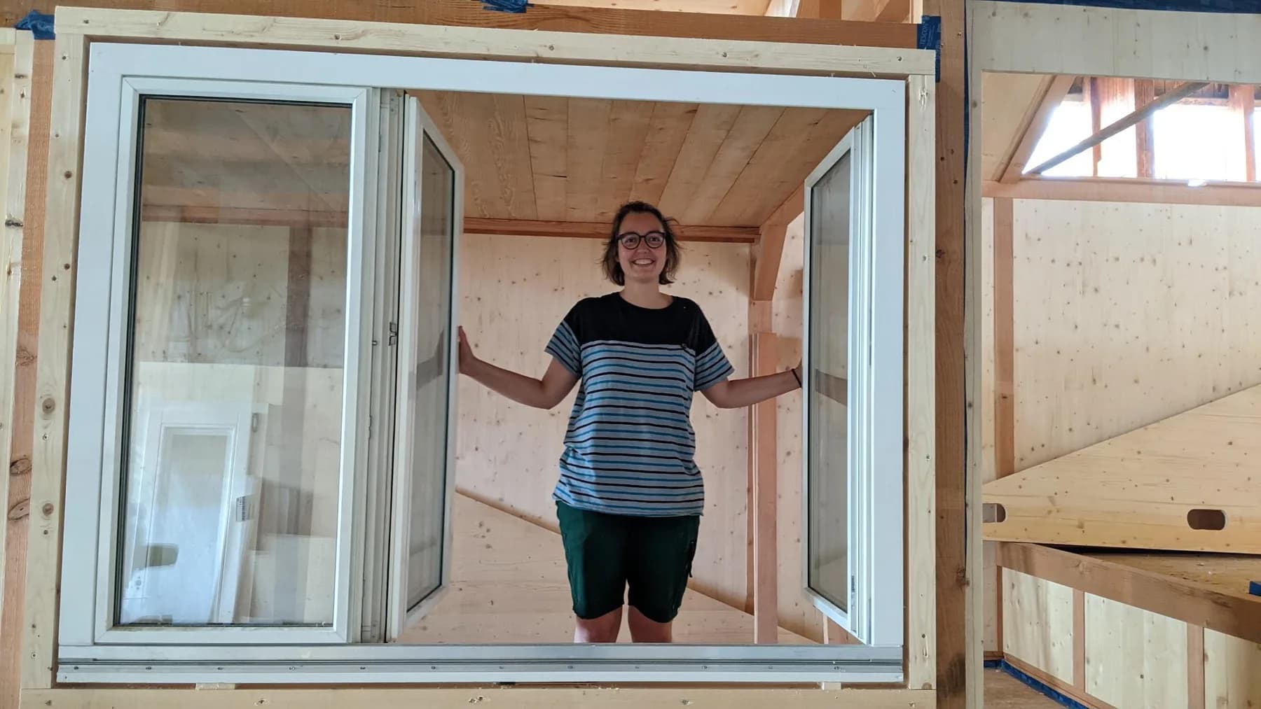 Sarah im Rohbau des Tiny House, die geöffneten Fensterflügel in den Händen